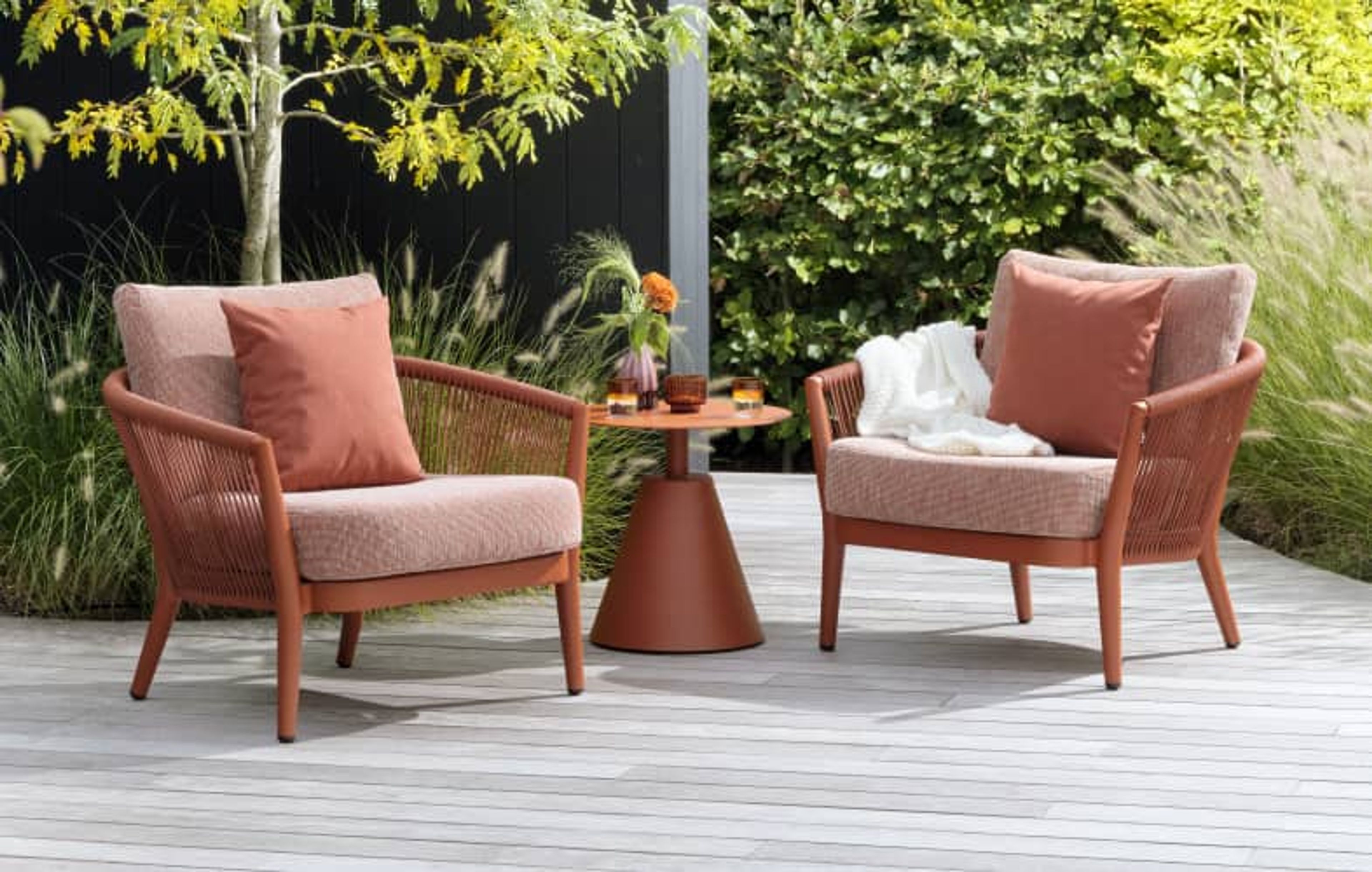 Een zonnig terras met een roestbruine Fano tafel en 4 Orso tuinstoelen.