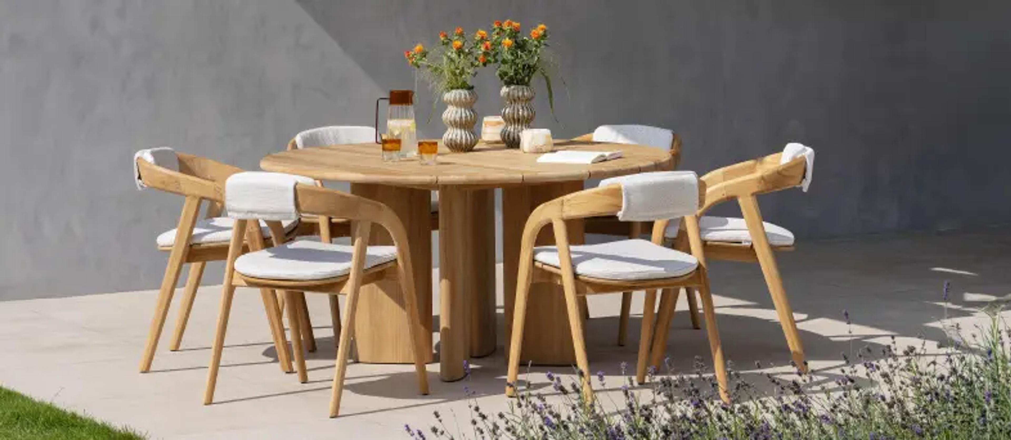 Een ronde teak tafel met 6 tuinstoelen op een zonnig terras van exterioo tuinmeubelen