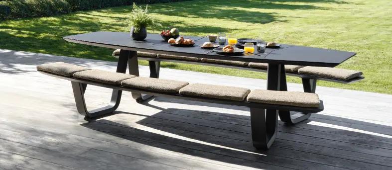 Een grote donkerkleurige picknick tafel in de schaduw op een terras van exterioo tuinmeubelen