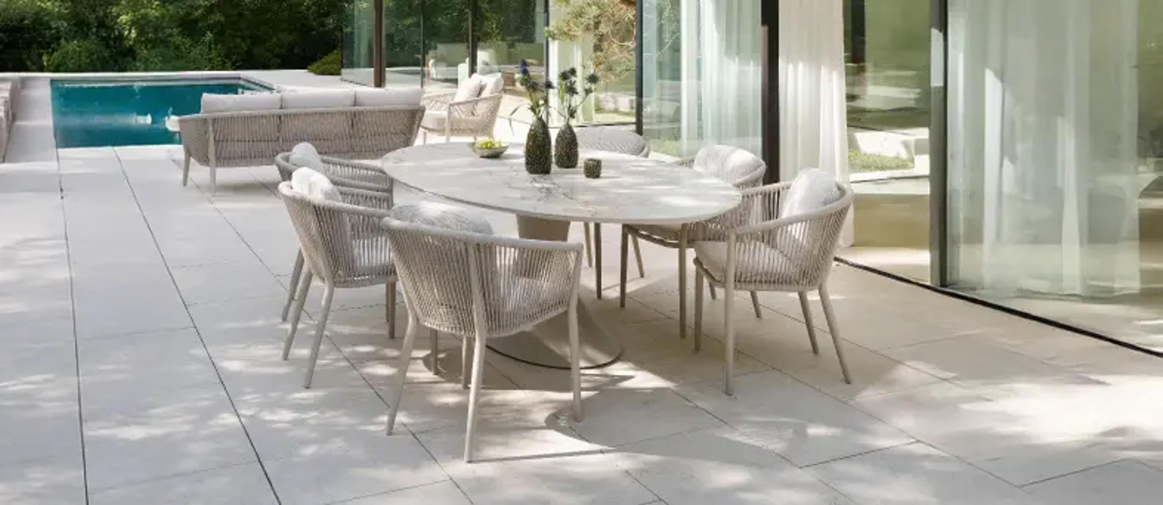Een beige tuintafel met tuinstoelen op een zonnig terras 